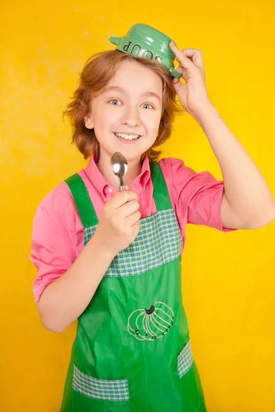 çorba tabağı ve bir kaşık ile yeşil mutfak önlük ayakta giyen güzel çocuk