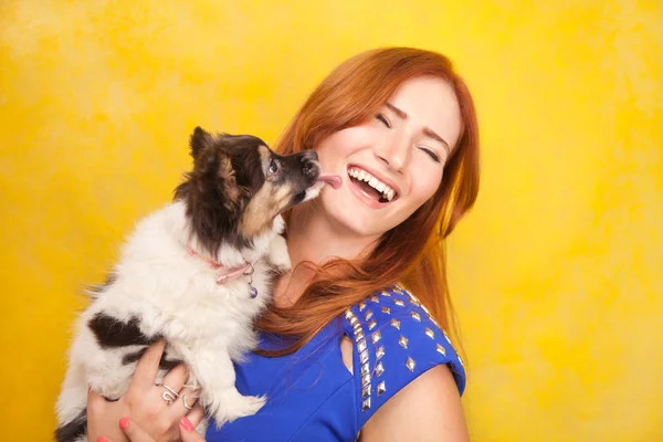 Bela redhaired jovem mulher de pé com pouco filhote de cachorro bonito no estúdio amarelo fundo — Fotografia de Stock