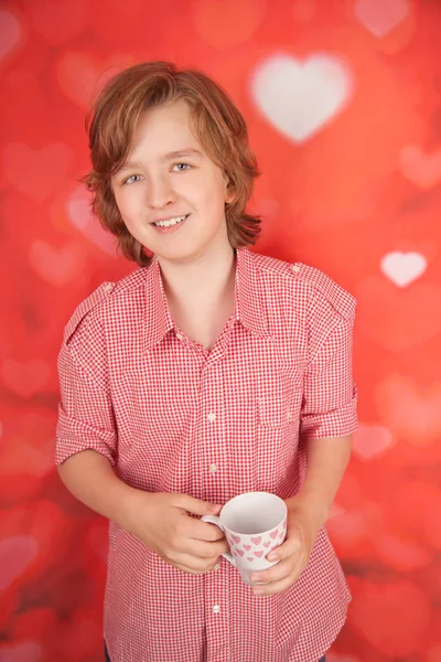 Schattige gelukkig lachend jongen met witte kop op rood hart studio achtergrond alleen — Stockfoto