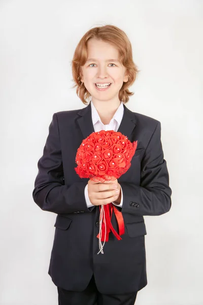 Roztomilý mladý teenager nošení obleku s červené kytice růže květy na bílém pozadí sám izolovaný — Stock fotografie