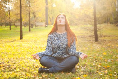 Sıcak Sonbahar lotus meditasyon poz sarı sonbahar parkta yere kazak tek başına oturmak giyen genç ve güzel kadın