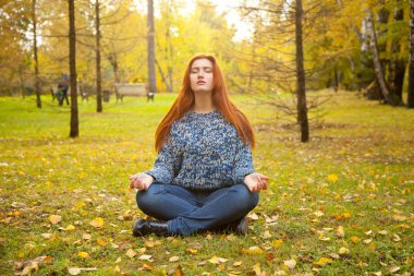 Sıcak Sonbahar lotus meditasyon poz sarı sonbahar parkta yere kazak tek başına oturmak giyen genç ve güzel kadın