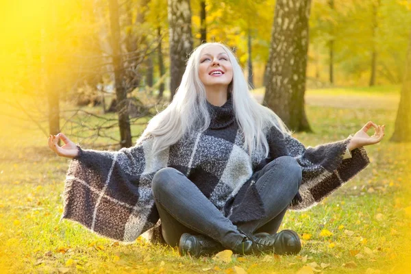 sıcak yün panço ve meditasyon rahatlama poz sonbahar parkta tek başına oturan kot giyen güzel sarışın kadın