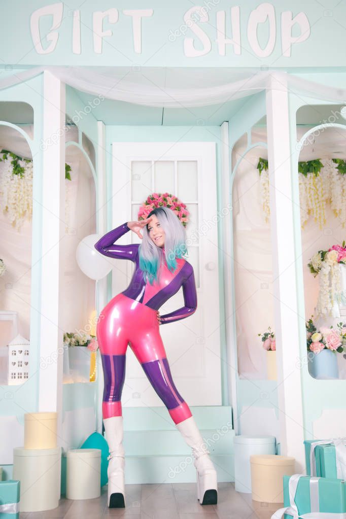 pretty anime girl wearing latex rubber doll catsuit and posing near cute white gift shop with air ballons and presents and gifts for christmas and new year