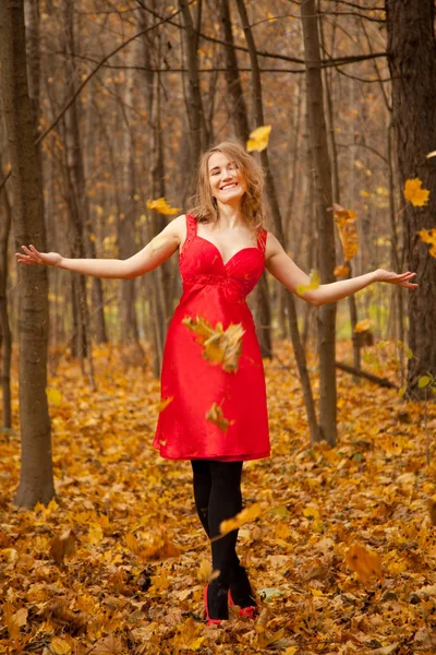 Bardzo modnej kobiety na sobie czerwoną sukienkę i osamotniony w lesie jesienią, rzucanie żółty spadek liści i zabawy — Zdjęcie stockowe