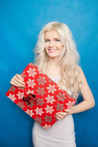 Bela mulher loira feliz vestindo vestido branco de pé com caixa de Natal presente vermelho no fundo do estúdio azul — Fotografia de Stock