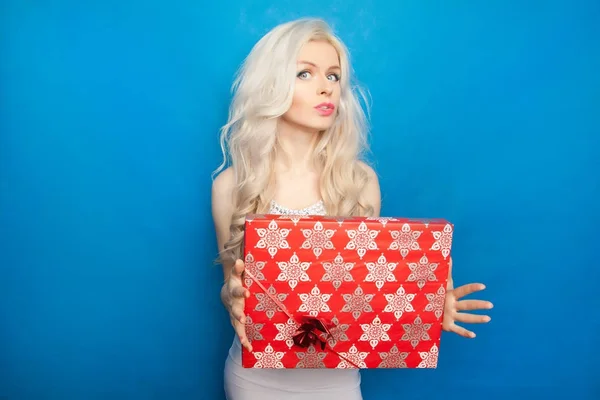 Krásné šťastné blond žena nosí stojící bílé šaty s červenými vánoční krabičky na modré studio pozadí — Stock fotografie