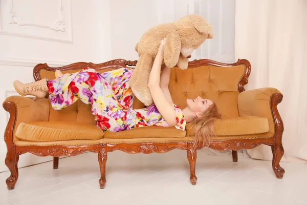 Pretty young caucasian woman with big brown teddy bear toy on the sofa — Stock Photo, Image