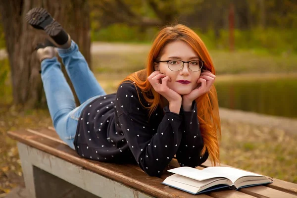 Menina ruiva bonita vestindo camisola bonito posando com um livro no parque sozinho — Fotografia de Stock