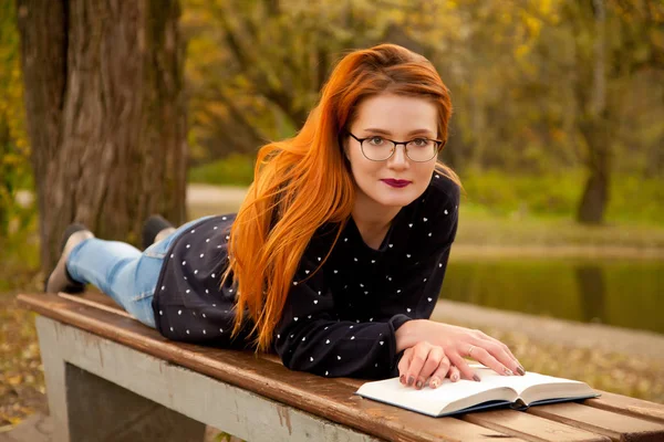 Menina ruiva bonita vestindo camisola bonito posando com um livro no parque sozinho — Fotografia de Stock
