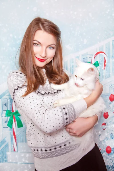 Bastante linda chica joven usando Navidad suéter blanco y de pie con gato doméstico solo en el fondo del estudio de año nuevo — Foto de Stock