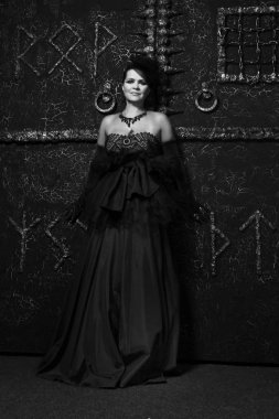 uzun bir gece elbisesi içinde güzel cadı arka plan siyah rune kapısı üzerinde duruyor 