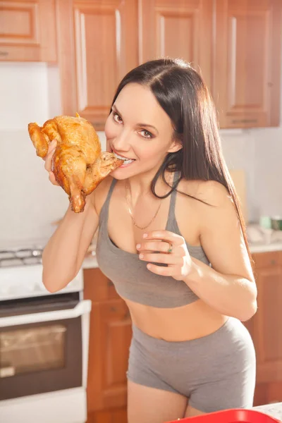 グレー スポーツ ホーム服ゴールデン フライ鶏肉を食べると一人で家で彼女のキッチンで朝の光窓の近くのテーブルに座って美しいフィットネス ブルネットの少女 — ストック写真