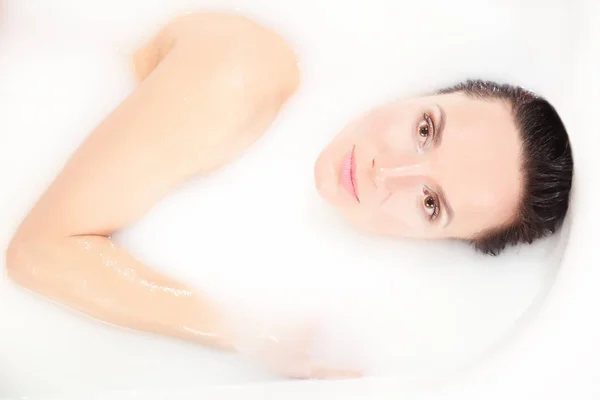 美丽的黑发女孩躺在浴缸里充满了牛奶 放松和得到快感 — 图库照片