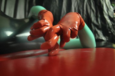 cute short-haired blonde girl posing in latex catsuit and rubber red gloves, alone on a dark background clipart