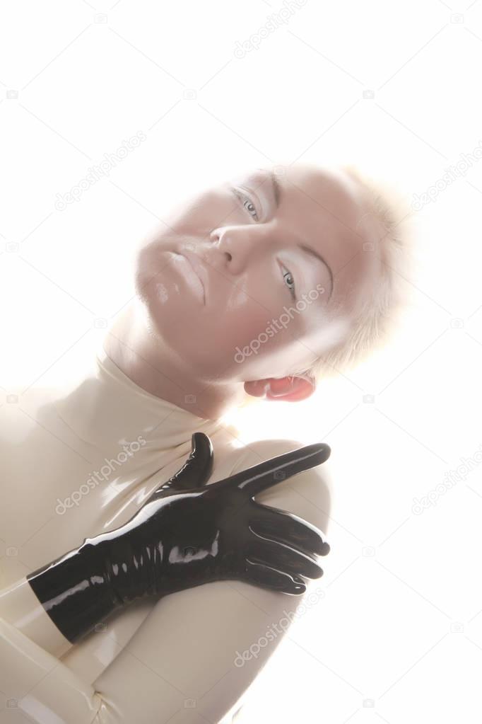strange futuristic alien albino woman with short blonde hair posing in latex rubber catsuit and tight corset with black gloves on white background isolated