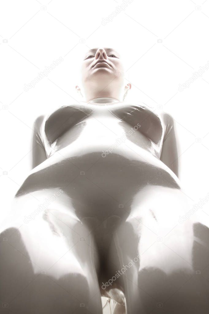 strange futuristic alien albino woman with short blonde hair posing in latex rubber catsuit and tight corset with black gloves on white background isolated