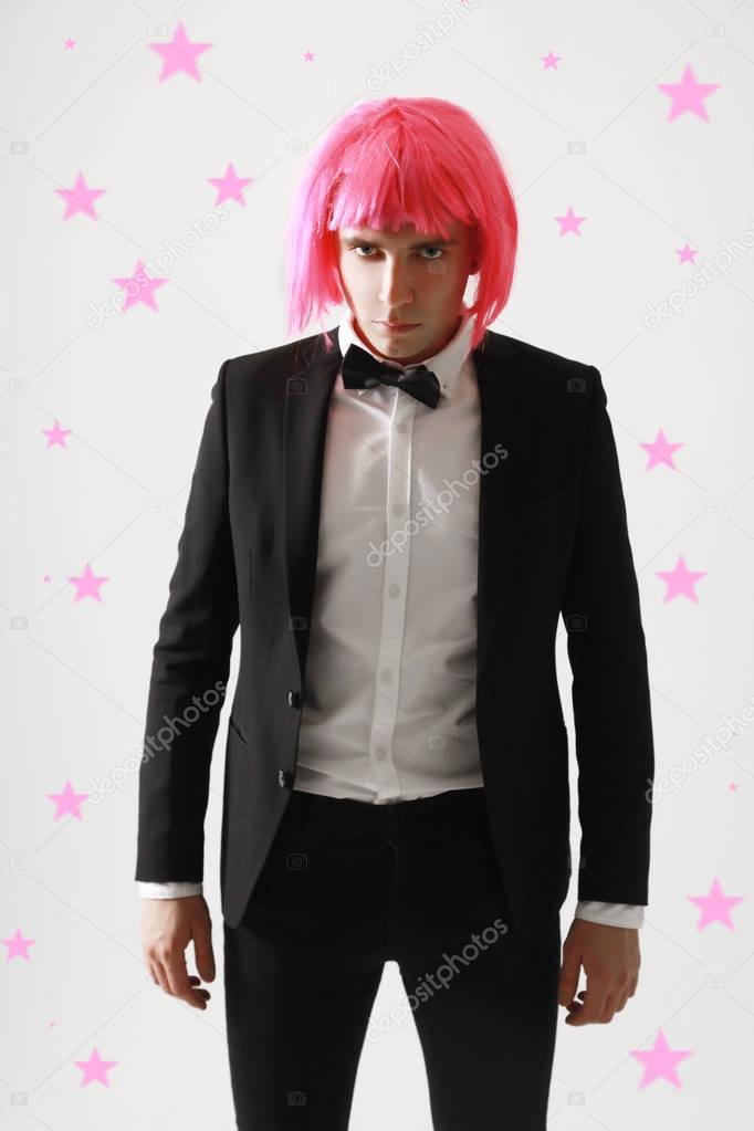 stylish and funny young guy standing in business suit and pink women wig on white background alone