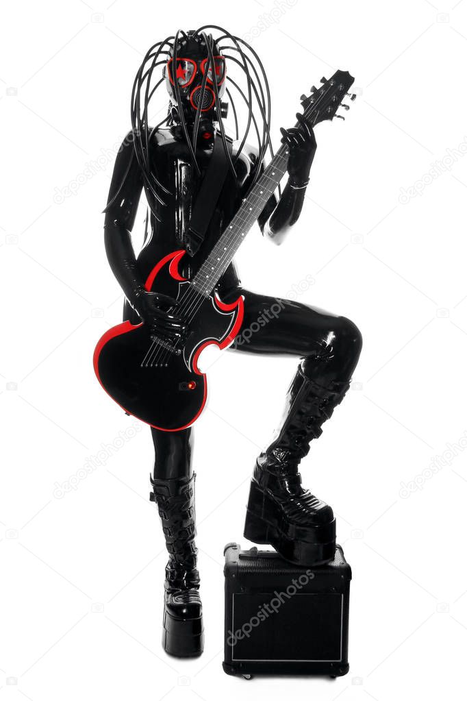 the rock musician woman in a black latex fetish suit and a gas mask stands with fashionable guitar on white background isolated