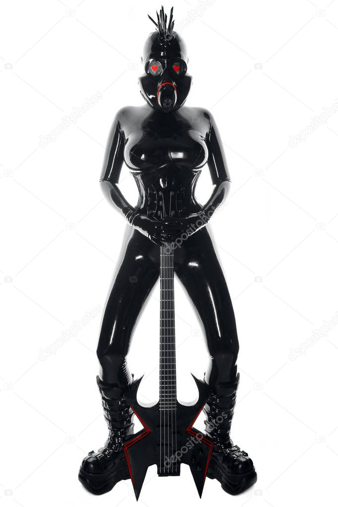 the rock musician woman in a black latex fetish suit and a gas mask stands with fashionable guitar on white background isolated