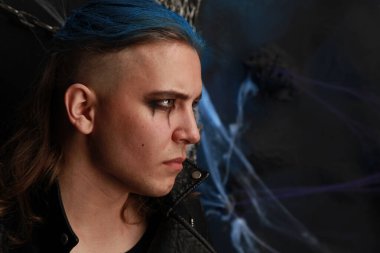 Siyah giyinmiş, siyah saçlı, mavi saçlı genç bir çocuk.