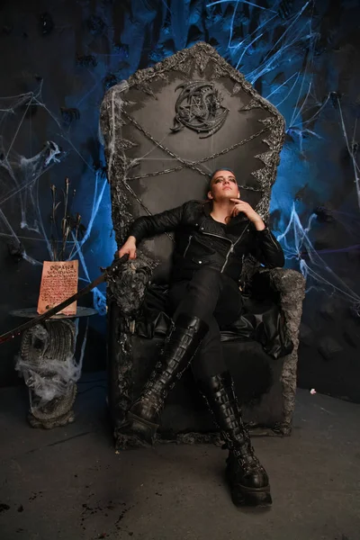Alternatieve vormgegeven jongeman zittend op de satan troon in donkere achtergrond alleen — Stockfoto