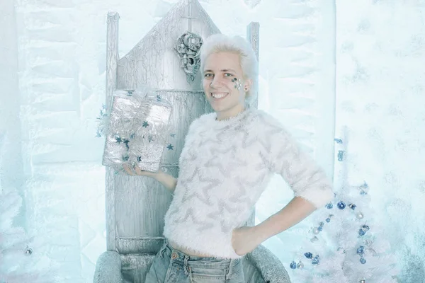 Navidad rubia caucásica chico en suéter blanco con estrellas celebración y regalo de apertura presente en la silla — Foto de Stock
