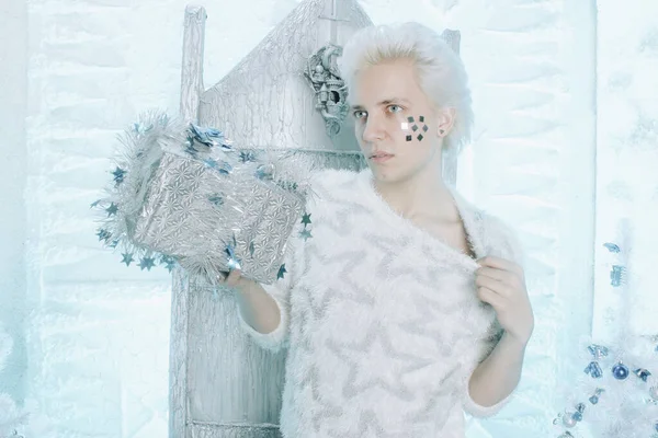 Navidad rubia caucásica chico en suéter blanco con estrellas celebración y regalo de apertura presente en la silla —  Fotos de Stock
