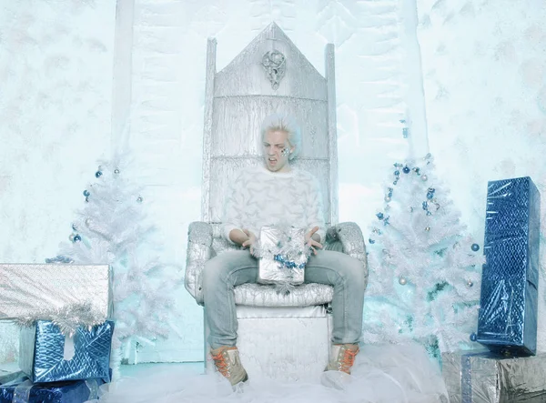 Navidad rubia caucásica chico en suéter blanco con estrellas celebración y regalo de apertura presente en la silla —  Fotos de Stock