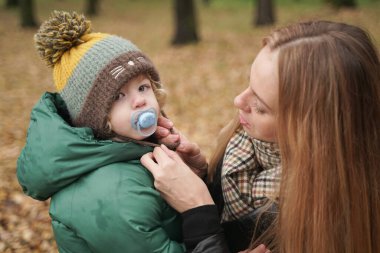 Annem sokaktaki bir çocuğa şapka takıyor. Neşeli küçük bebek portresi moda annesiyle dışarıda eğleniyor.