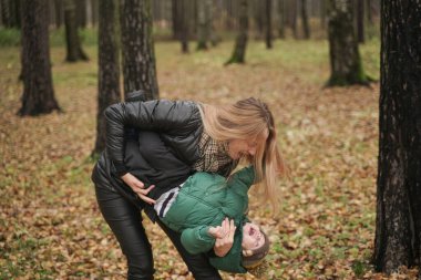 Güzel beyaz anne ve küçük çocuk sonbahar parkında eğleniyor, yürüyor. Anne çocuğu kollarında tutuyor.