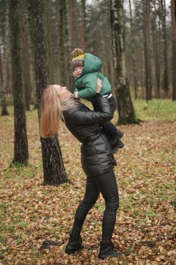 Güzel beyaz anne ve küçük çocuk sonbahar parkında eğleniyor, yürüyor. Anne çocuğu kollarında tutuyor.