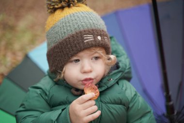 Parkta renkli gökkuşağı şemsiyeli tanınmayan küçük bir çocuk. 2 yaşındaki bebek, sonbaharda ceket ve şapka giyer.