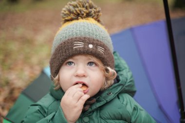 Parkta renkli gökkuşağı şemsiyeli tanınmayan küçük bir çocuk. 2 yaşındaki bebek, sonbaharda ceket ve şapka giyer.