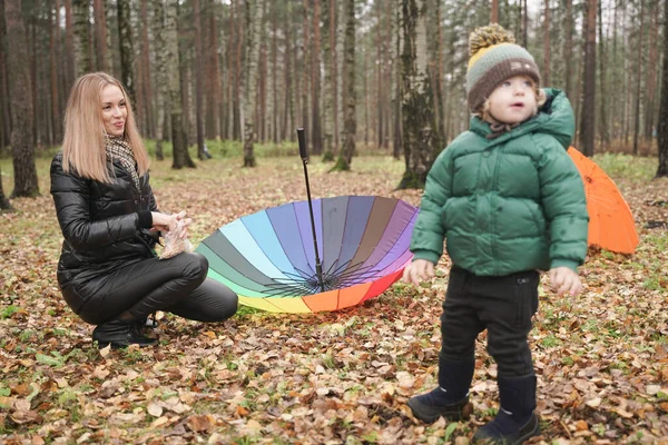 Une belle mère caucasienne et un petit enfant s'amusent dans le parc d'automne, marchant avec un parapluie — Photo
