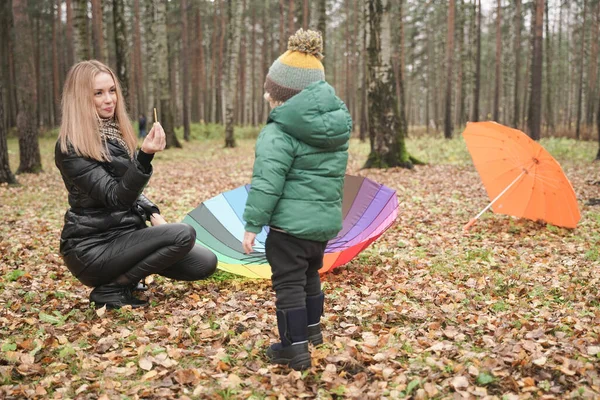 Uma bela mãe caucasiana e criança pequena se divertindo no outono Park, andando com guarda-chuva — Fotografia de Stock