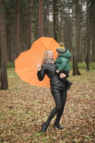 Uma bela mãe caucasiana e criança pequena se divertindo no outono Park, andando com guarda-chuva — Fotografia de Stock