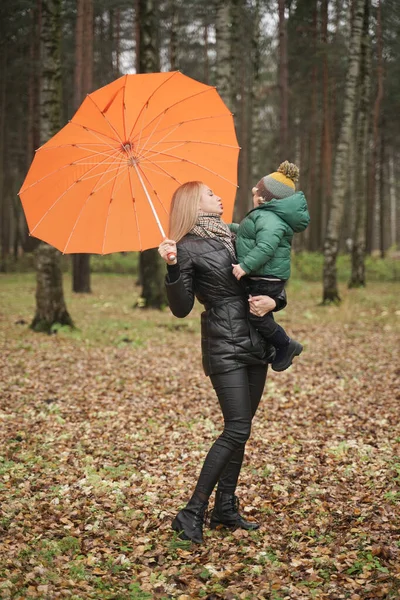 Uma bela mãe caucasiana e criança pequena se divertindo no outono Park, andando com guarda-chuva — Fotografia de Stock