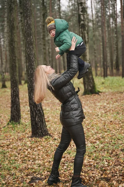 Bela mãe caucasiana e criança pequena se divertindo no outono Parque, andando. mãe segura a criança em seus braços — Fotografia de Stock