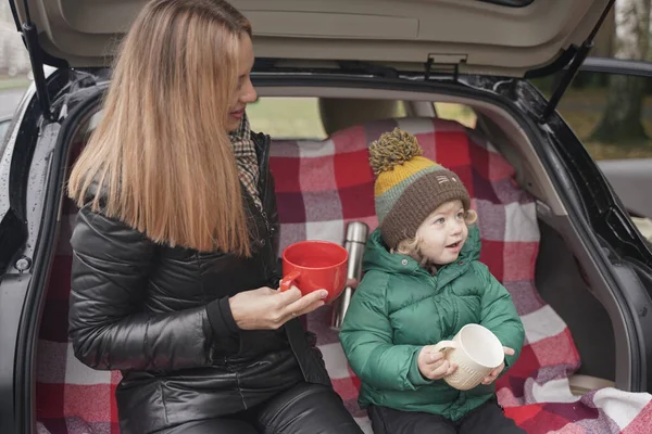 Family adventure - family on autumn camp. Young beauty mom and little child had picnic in back of car near the fall park