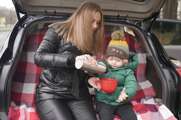 Family adventure - family on autumn camp. Young beauty mom and little child had picnic in back of car near the fall park