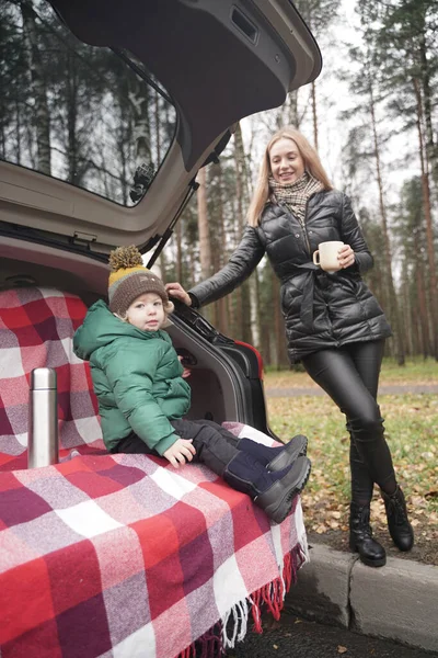 Family adventure - family on autumn camp. Young beauty mom and little child had picnic in back of car near the fall park