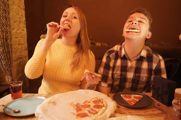 快乐的怀孕妇女，与十几岁的男孩一起吃披萨，并享受它的味道。 朋友们喜欢快餐。 在比萨饼店吃饭. — 图库照片