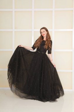 Moda dünyasından zarif, ince, yetişkin bir kadın. Uzun, dantelli, siyah bir elbise. Beyaz stüdyo arka planında.