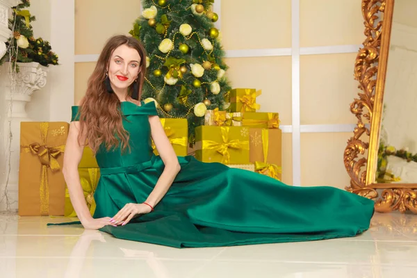 Bella donna snella allegra in abito da sera verde lungo celebrare il Natale in camera bianca decorata vicino al grande specchio d'oro. corpo a tutta lunghezza — Foto Stock