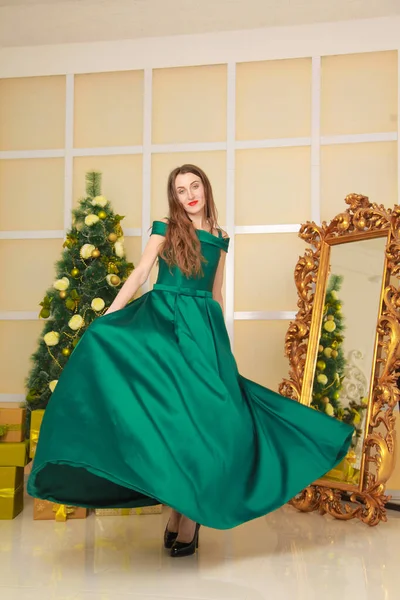 Hermosa mujer delgada alegre en vestido de noche verde largo celebrar la Navidad en la habitación blanca decorada cerca del espejo de oro grande. cuerpo de longitud completa — Foto de Stock