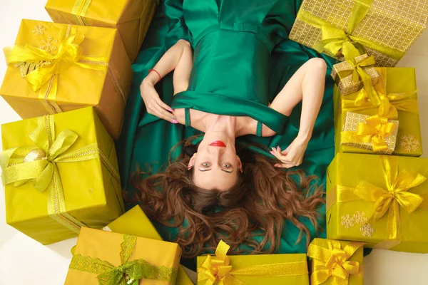 top view of beautiful slender fashion woman in trendy green dress lying with golden boxes with gifts. cheerful girl ready to celebrate christmas.