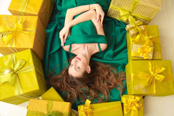 top view of beautiful slender fashion woman in trendy green dress lying with golden boxes with gifts. cheerful girl ready to celebrate christmas.