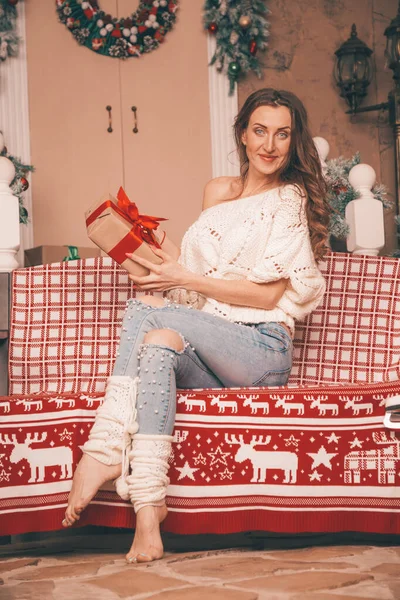 Чарівна тонка дівчина в модних джинсах вишита перлами і різдвяним светром босоніж сидить на лавці, повноцінне тіло — стокове фото