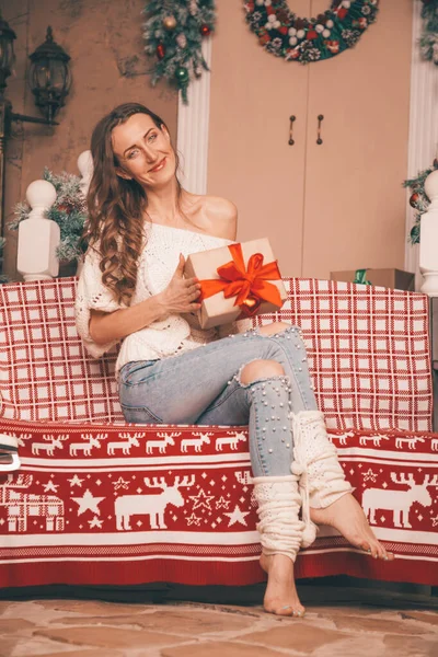 Чарівна тонка дівчина в модних джинсах вишита перлами і різдвяним светром босоніж сидить на лавці, повноцінне тіло — стокове фото